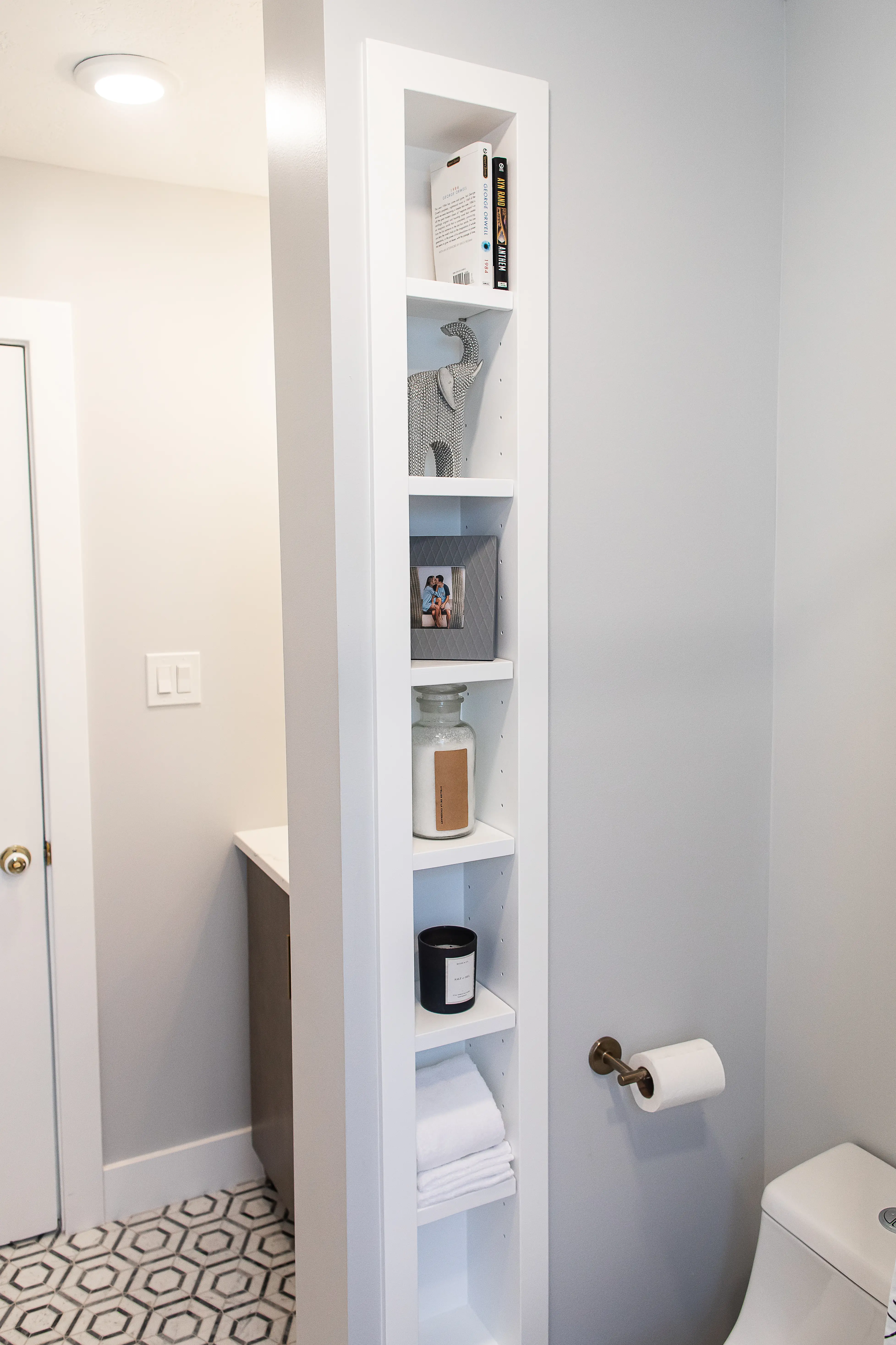 A small bathroom with built in shelving near the toilet. 