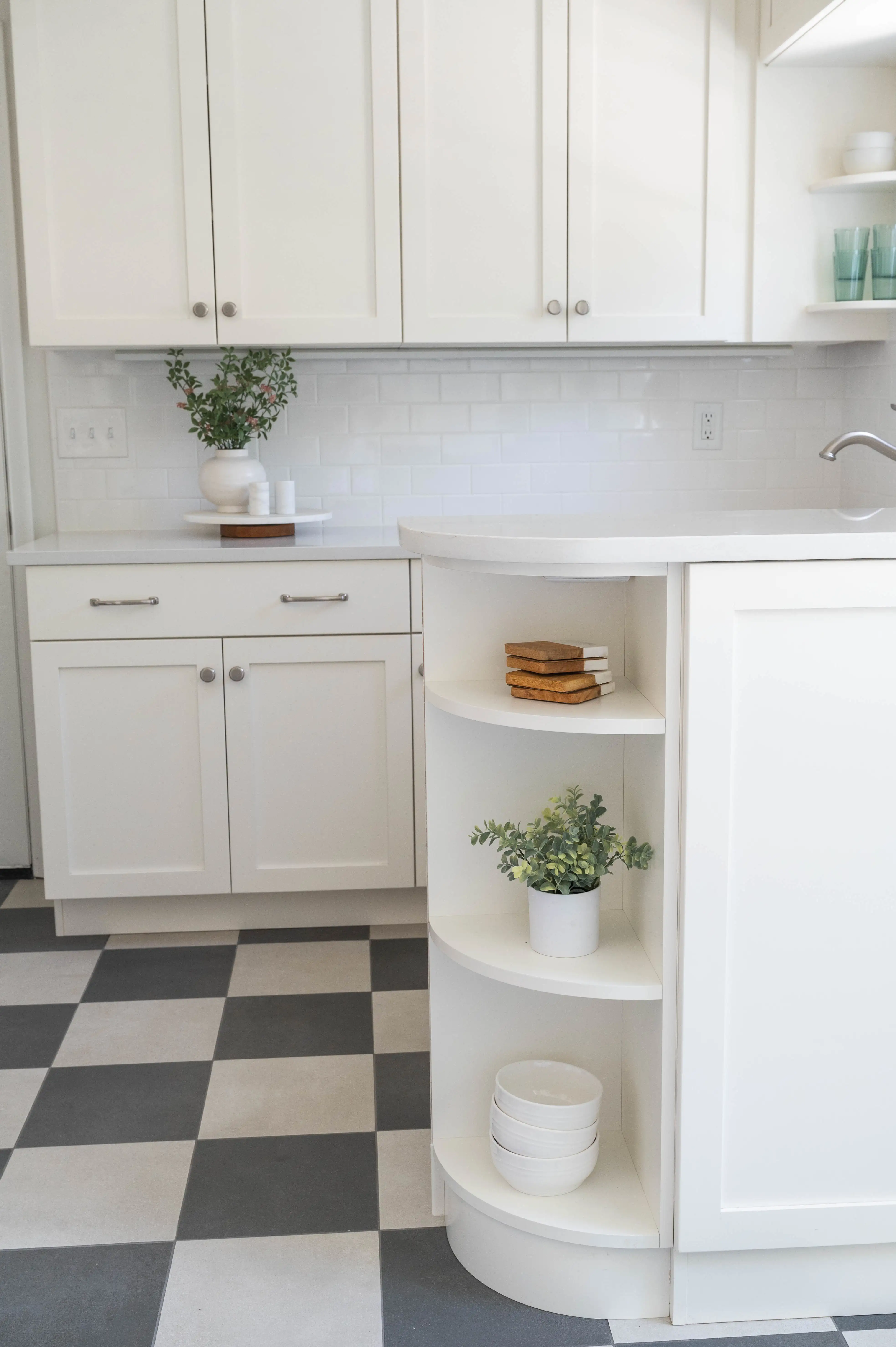 A kitchen with white cabinets and countertops. Stainless steel handles and hardware throughout. The flooring is a black and white tile. The backsplash is a white subway tile. 