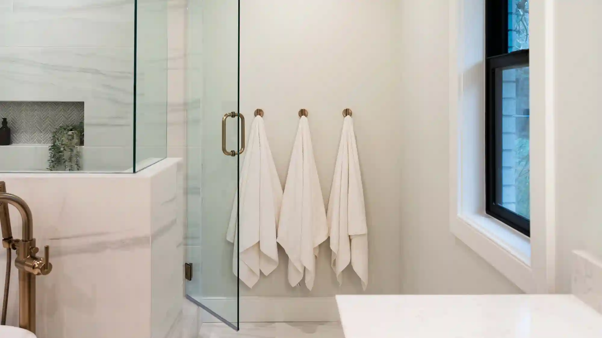 Primary bathroom, large walk in shower to the left, three towel hooks and towels on back wall and a large window on the right hand wall. 