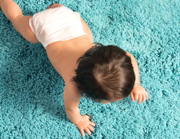 A baby in a white diaper crawling on a bright blue fuzzy carpet, viewed from above.