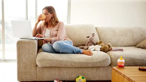 Woman sitting comfortably on the couch working on her laptop while drinking coffee