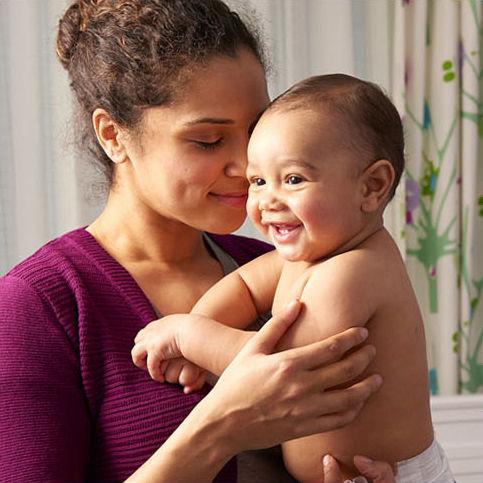 A smiling mother cradles her happy baby in her arms, both sharing a tender moment.