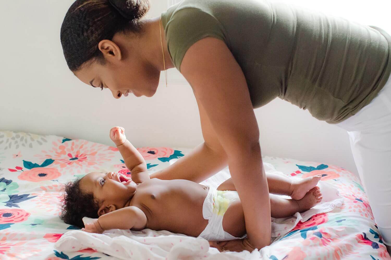 woman smiling at baby laying on a bed