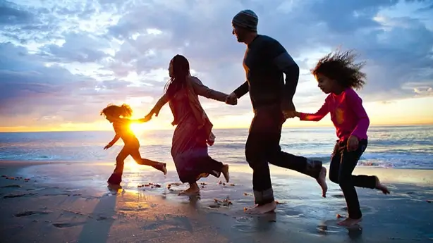 Two adults and two children at the beach running barefoot together in the wet sand