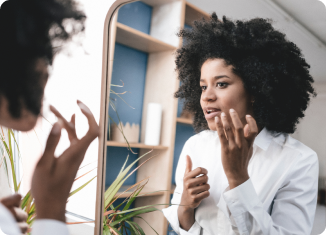 A woman with curly hair looking in a mirror and applying lip balm to treat chapped lips.