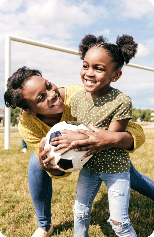 Mother playing outside with a soccer ball with her daughter.