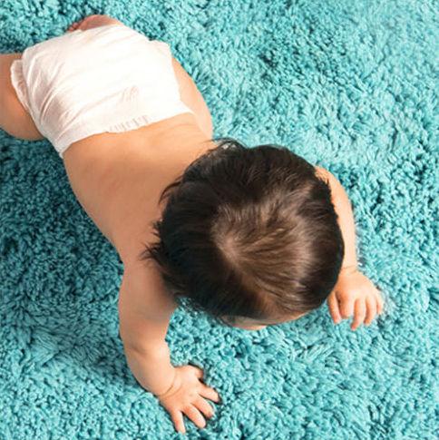 A baby in a white diaper crawling on a bright blue fuzzy carpet, viewed from above.