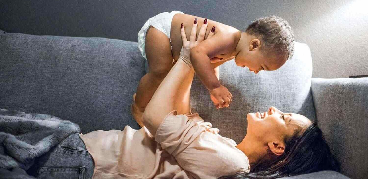 woman on a couch holding baby in the air