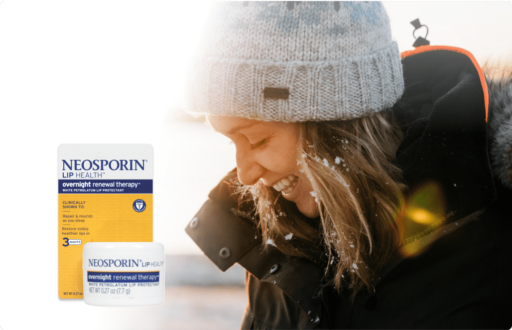 Smiling woman in a winter coat and beanie, with Neosporin Lip Health Overnight Renewal Therapy product in the foreground.