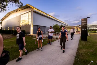 Group of people walking along a path near a modern building at dusk.