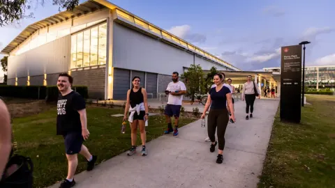 Group of people walking along a path near a modern building at dusk.