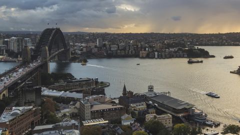 Panoramic view of sydney skyline featuring the harbour bridge and opera house with a stormy sky in the background.