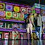 Two people walk hand in hand at night in front of a building illuminated with colorful, geometric light projections.