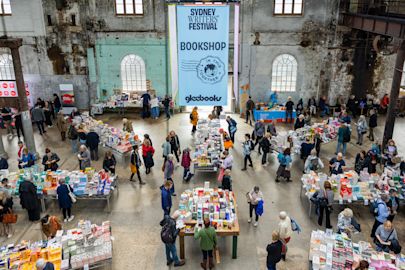 People browse tables of books at the Sydney Writers’ Festival bookshop inside a large industrial-style hall with high windows.