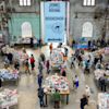 People browse tables of books at the Sydney Writers’ Festival bookshop inside a large industrial-style hall with high windows.