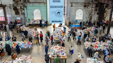 People browse tables of books at the Sydney Writers’ Festival bookshop inside a large industrial-style hall with high windows.