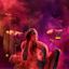 An Aboriginal dancer crouches low on stage over a cultural fire of smoking Eucalyptus leaves, cast in moody red and purple light