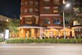 People dine outside under orange umbrellas at a restaurant on the ground floor of a curved brick building at night.