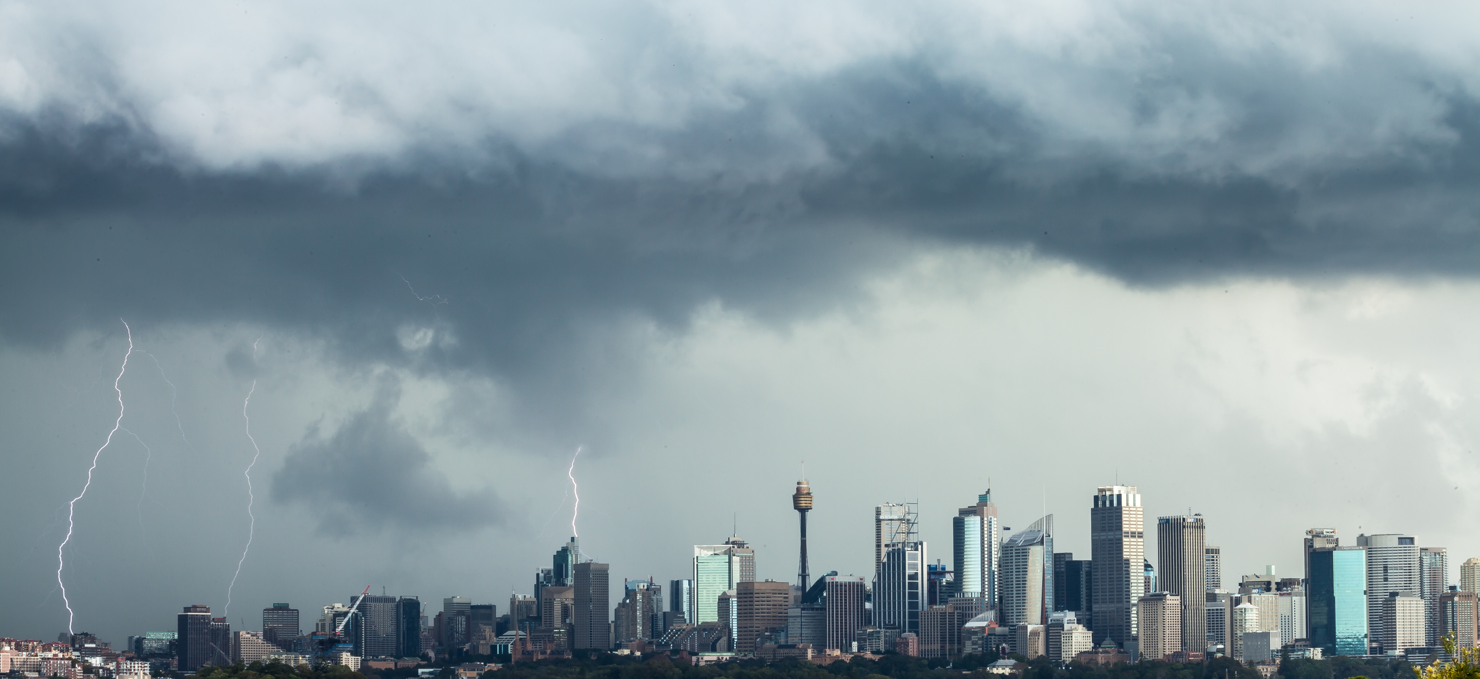 Image description: Dark storm clouds and bolts of lightning hang over the Sydney skyline.