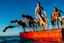 A group of people in swimwear jump and dive off a red floating platform into the water under a clear blue sky.