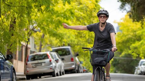 A woman signals to turn while on a bike in a suburban street in Syndey