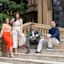 Four adults pose together on outdoor marble steps in front of a historic building with arched windows and lush greenery.