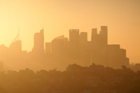 City skyline silhouetted against a hazy, golden sunrise, with tall buildings and a soft, warm glow in the sky.