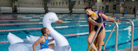 Two people enjoying leisure time at an indoor swimming pool with an inflatable swan.