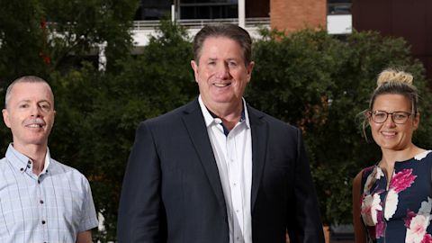 Two men and one young woman standing in the courtyard of an apartment complex, St Margaret's, in Surry Hills
