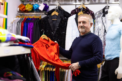 A man in a clothing store holding a red shirt with colorful sparkly jackets and shirts hanging on racks in the background.