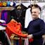 A man in a clothing store holding a red shirt with colorful sparkly jackets and shirts hanging on racks in the background.