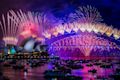 Fireworks illuminate the night sky over the Sydney Opera House and Sydney Harbour Bridge, with boats on the water.