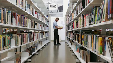 A man reads a book while standing in between the shelves at Kings Cross library