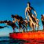 A group of people in swimwear jump and dive off a red platform into the water under a clear blue sky.