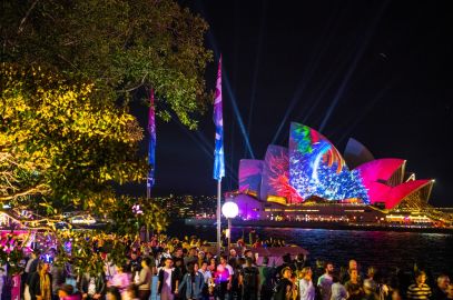 Crowd of people at a nighttime outdoor event with colorful light projections on the sydney opera house.