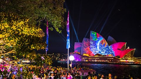 Crowd of people at a nighttime outdoor event with colorful light projections on the sydney opera house.