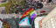 Aerial view of the Bourke and Campbell Street intersection in Darlinghurst painted with a Progress Pride flag, with pedestrians walking nearby, a red car parked on the side, and buildings and trees in the surroundings.