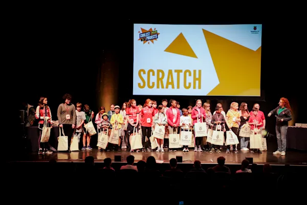 A large group of young people stand on stage collecting prizes from a judge.