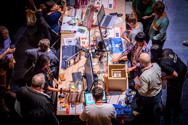 A photo taken from above of a table full of computers and hardware projects, surrounded by young creators and judges, at a coolest projects live event
