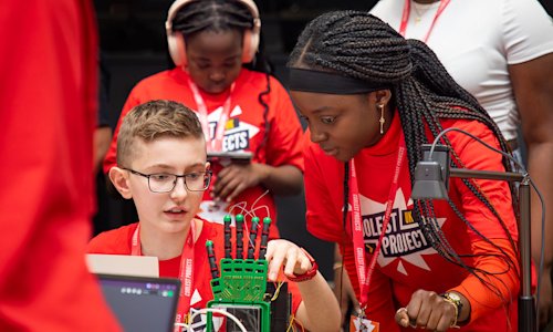 Two young people look at a robotic hand project.