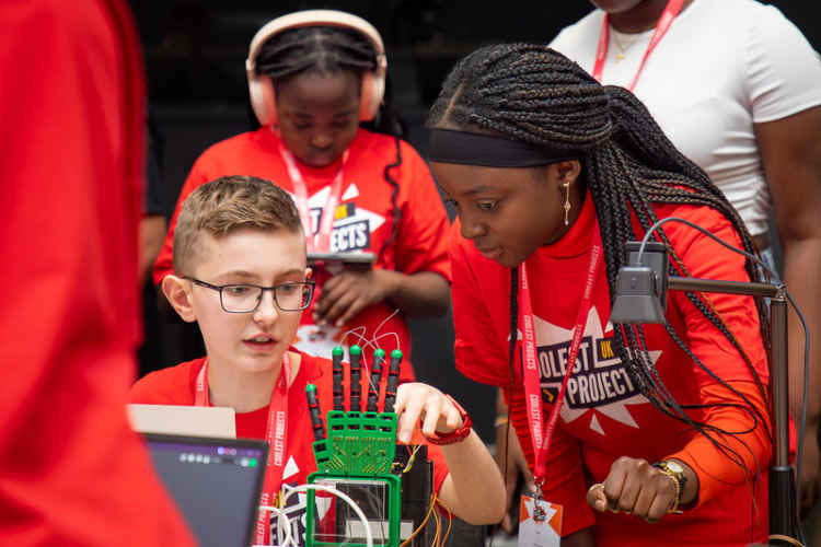 Two young people look at a robotic hand project.