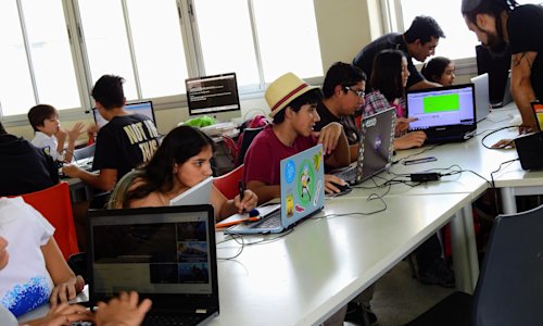 A group of young people look at laptops.