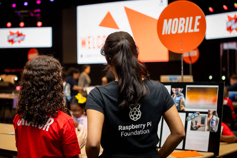 A young girl shows her mobile app project to a judge in a black t-shirt.