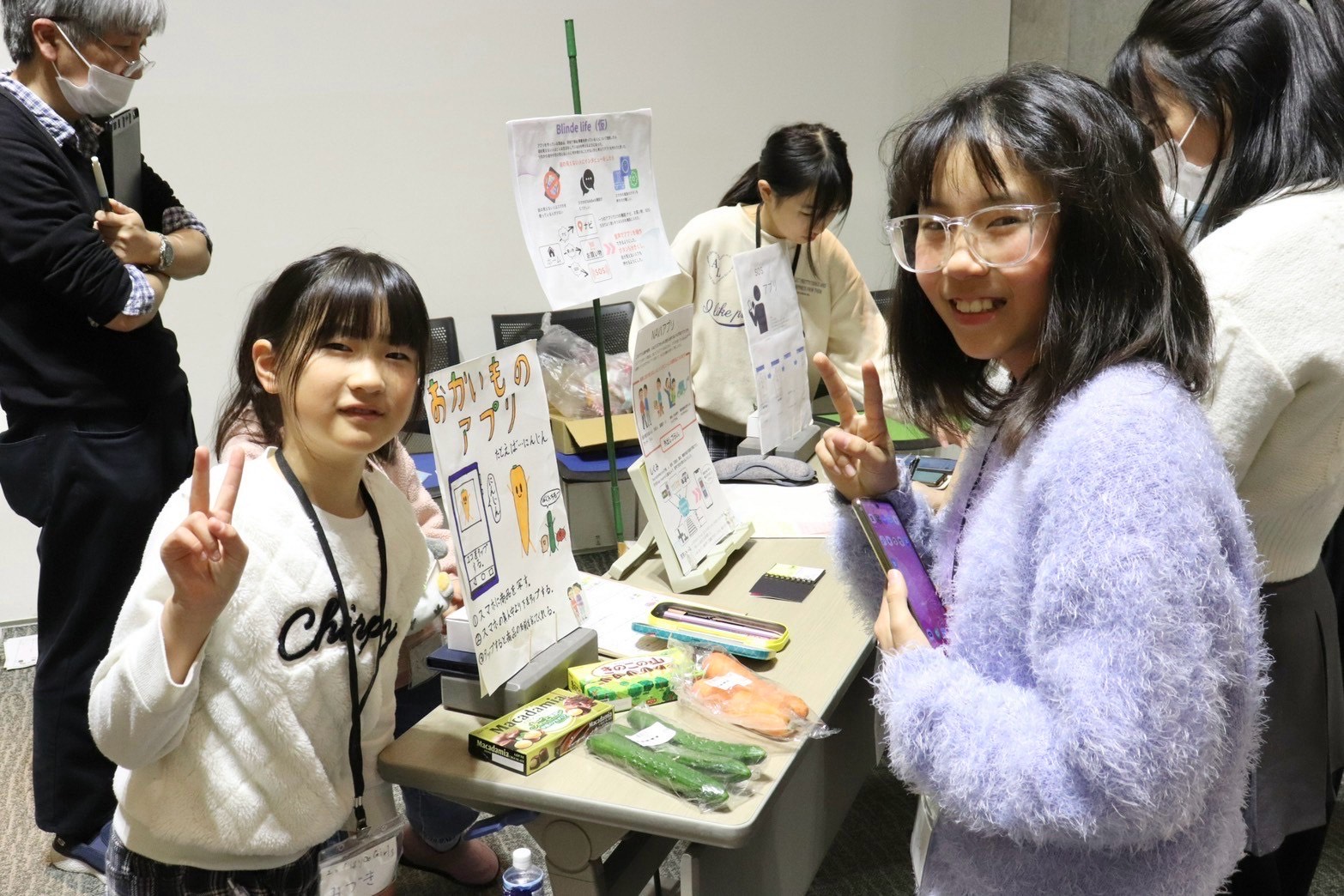 Two girls display posters about their computing project at a busy event.