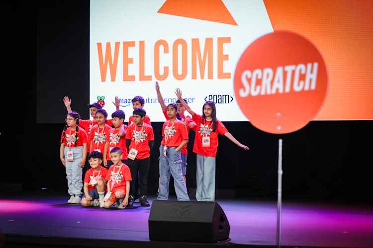 Young people pose on stage under a large sign saying "welcome".