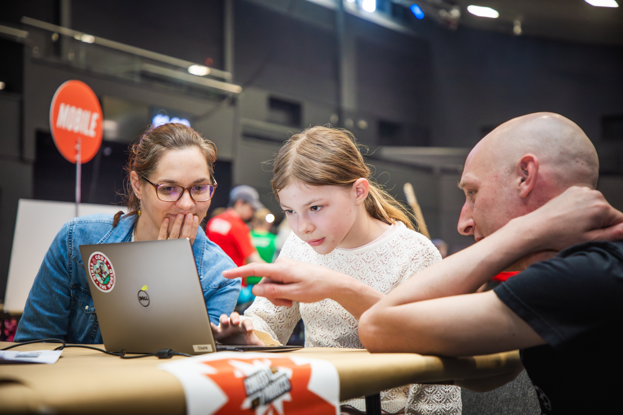 "A participant and two mentors looking at a mobile app project at Coolest Projects UK"