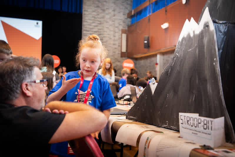 A girl shows her coding project to a judge at an event.