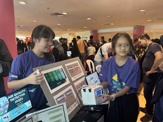 Two young girls show their computing project at a busy event.