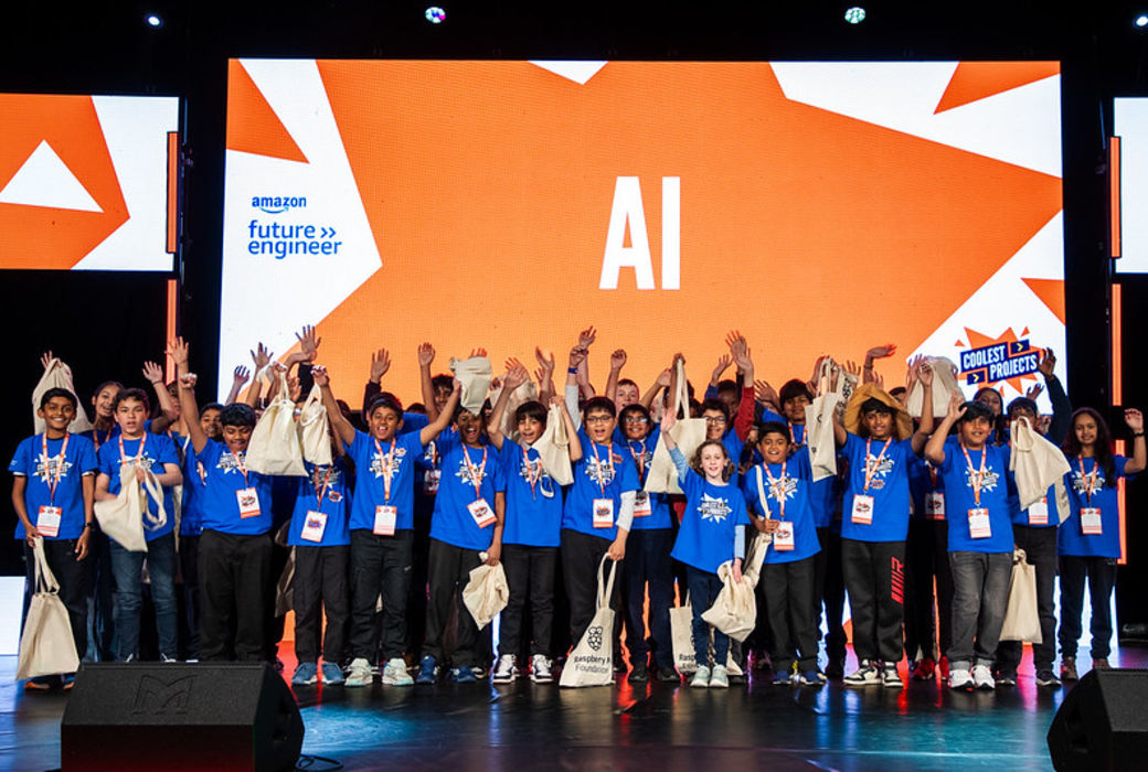 A group of young people in blue t-shirts cheer on stage.