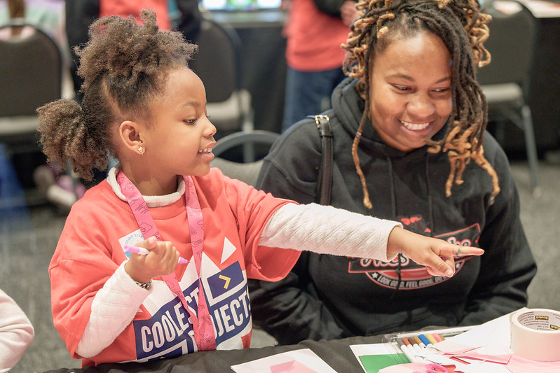 A young girl shows her computing project to a teacher.